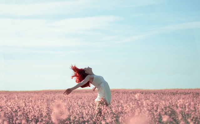 femme libre dans un champ penchée en arrière les bras écartés et cheveux au vent