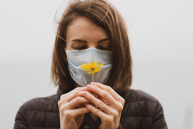 femme portant un masque et sentant une fleur jaune