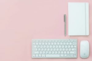 bureau rose sur lequel est posé un clavier, une souris, un cahier et un stylo
